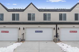 View of front of home with stucco siding, ac unit, an attached garage, and driveway