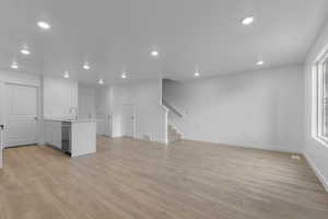 Unfurnished living room featuring light wood-style floors, recessed lighting, stairway, baseboards, and a sink