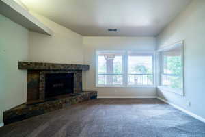 Unfurnished living room featuring healthy amount of natural light, baseboards, carpet flooring, and a fireplace with raised hearth