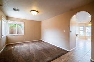 Carpeted spare room with a textured ceiling, arched walkways, and baseboards