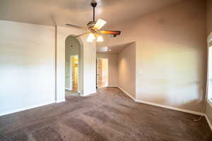 Spare room with carpet, ceiling fan, arched walkways, and baseboards