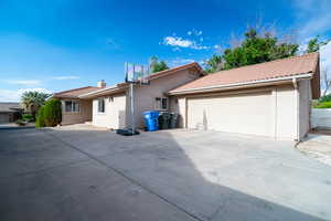 View of side of property with stucco siding, a tile roof, a garage, concrete driveway, and a chimney