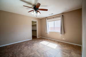 Unfurnished bedroom with baseboards, a walk in closet, a closet, and a ceiling fan