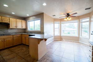 Kitchen featuring a sink, a peninsula, a textured ceiling, under cabinet range hood, and recessed lighting