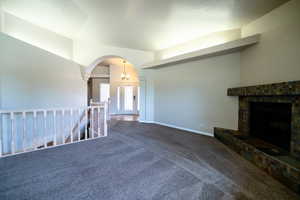 Unfurnished living room with carpet floors, a fireplace with raised hearth, arched walkways, and baseboards