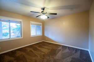 Spare room featuring dark colored carpet, baseboards, and ceiling fan