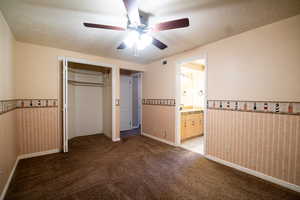Unfurnished bedroom featuring light colored carpet, a wainscoted wall, a textured ceiling, a closet, and a sink