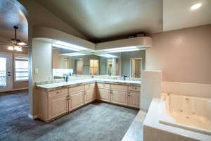 Full bath with vaulted ceiling, a whirlpool tub, double vanity, a ceiling fan, and baseboards