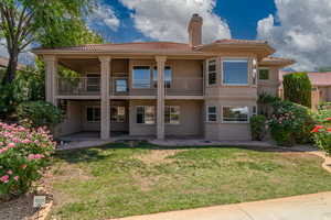 Rear view of property with a balcony, a tile roof, stucco siding, a chimney, and a yard