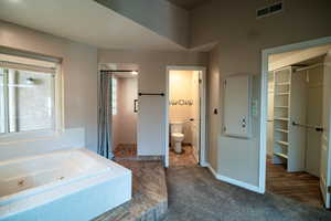 Bathroom featuring tiled shower, a jetted tub, toilet, a walk in closet, and baseboards