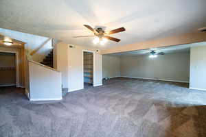 Unfurnished living room featuring a ceiling fan, carpet flooring, stairs, baseboards, and a textured ceiling