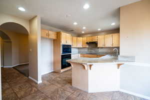 Kitchen featuring black appliances, a peninsula, under cabinet range hood, a sink, and arched walkways
