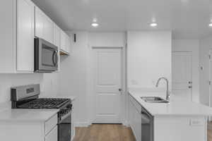 Kitchen with stainless steel appliances, a sink, a peninsula, light wood-style flooring, and light countertops