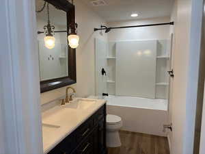 Full bathroom with wood finished floors, toilet, double vanity, and washtub / shower combination