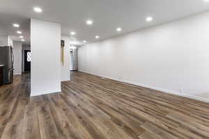 Unfurnished living room featuring dark wood finished floors, baseboards, recessed lighting, and a chandelier