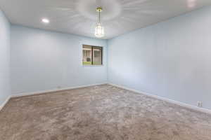 Carpeted empty room with baseboards, recessed lighting, and a chandelier