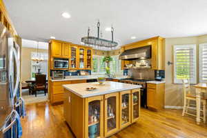 Kitchen with wall chimney exhaust hood, stainless steel appliances, light countertops, light wood-type flooring, and a textured ceiling
