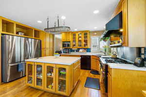 Kitchen with stainless steel appliances, open shelves, ventilation hood, light countertops, and light wood finished floors