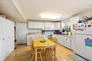 Kitchen featuring white appliances, washer and clothes dryer, light wood-style flooring, white cabinetry, and light countertops