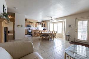 Dining space with light tile patterned floors, baseboards, ceiling fan, a textured ceiling, and a fireplace