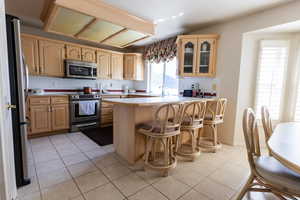 Kitchen featuring appliances with stainless steel finishes, a peninsula, light countertops, light brown cabinets, and glass insert cabinets