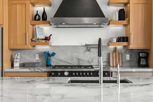 Kitchen with backsplash, wall chimney range hood, open shelves, and light stone countertops