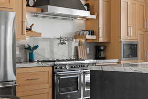Kitchen featuring black appliances, ventilation hood, light stone countertops, and tasteful backsplash
