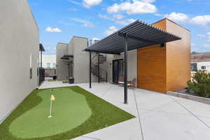 Back of house with stucco siding, a pergola, a patio, and a putting green