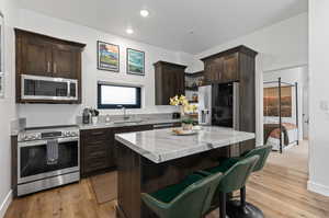 Kitchen featuring stainless steel appliances, dark wood finish cabinets, a breakfast bar, light stone countertops, and light wood-style floors