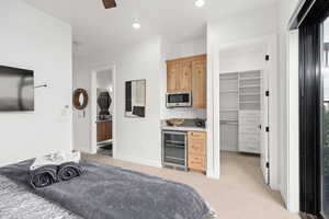 Bedroom featuring light carpet, a walk in closet, wine cooler, ceiling fan, and connected bathroom