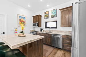 Kitchen featuring appliances with stainless steel finishes, light wood-style floors, a kitchen island, dark brown cabinets, and a breakfast bar