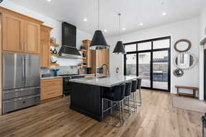 Kitchen with high end appliances, light stone counters, decorative light fixtures, an island with sink, and dual tone cabinets