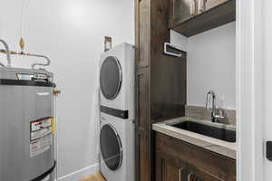 Laundry area featuring water heater, stacked washer and dryer, and cabinet space