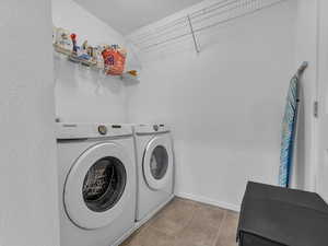 Clothes washing area featuring washer and clothes dryer, laundry area, baseboards, and light tile patterned floors