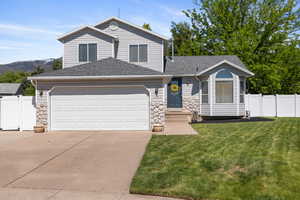 View of front facade featuring concrete driveway, roof with shingles, an attached garage, and stone siding