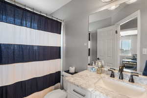 Bathroom with toilet, vanity, and curtained shower