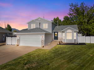 View of front of home featuring an attached garage, driveway, a shingled roof, stone siding, and a gate