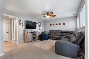 Living area with light carpet, a ceiling fan, baseboards, and light tile patterned floors