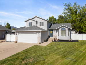 Tri-level home featuring a garage, concrete driveway, a shingled roof, and stone siding