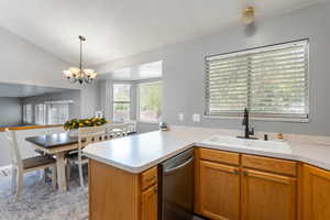 Kitchen featuring a sink, dishwasher, light countertops, a chandelier, and lofted ceiling