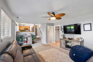 Living room with a chandelier, stairway, light colored carpet, a textured ceiling, and ceiling fan