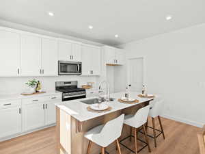 Kitchen with appliances with stainless steel finishes, a sink, light wood finished floors, a kitchen bar, and white cabinets