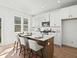 Kitchen with appliances with stainless steel finishes, a sink, light wood finished floors, a center island with sink, and recessed lighting