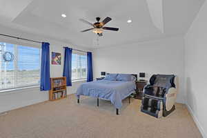 Owners suite with view of the lake, try ceiling and attached Grand Owners Bedroom  carpet,, recessed lighting, and a ceiling fan