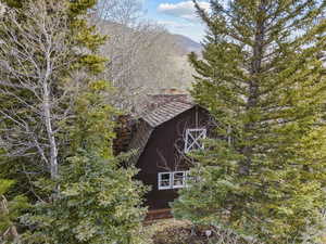 View of side of home featuring a barn, a chimney, a mountain view, and an outbuilding