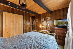 Carpeted bedroom featuring beamed ceiling, wooden ceiling, and wooden walls