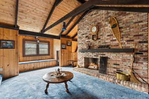 Living room featuring carpet floors, wooden walls, wooden ceiling, and a brick fireplace