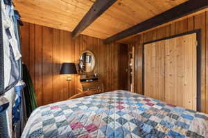 Bedroom featuring wooden ceiling, beam ceiling, and wooden walls