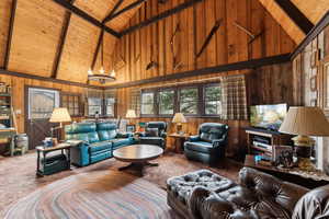 Living room featuring high vaulted ceiling, wooden ceiling, wooden walls, carpet, and beamed ceiling