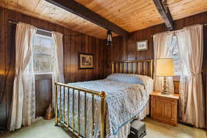 Carpeted bedroom with beam ceiling, wooden ceiling, and wood walls